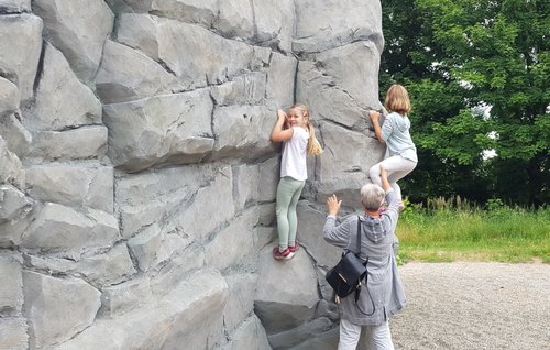 Zwei Mädchen an der Kletterwand und eine erwachsene Person sichert sie ab